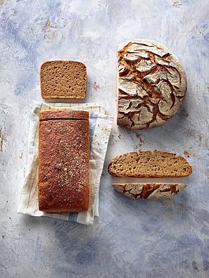 Das runde Weizenmischbrot mit rustikal aufgerissener, bemehlter Kruste und hellbraun gefärbter, kleinporiger Krume (rechts) liegt neben dem dunkelbraun ausgebackenen, kastenförmigen Weizenvollkornmischbrot mit glatter Oberfläche und mittelbraun gefärbter, lockerer Krume (links).