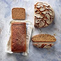 Das dunkelbraun ausgebackene, kastenförmige Weizenvollkornmischbrot mit glatter Oberfläche und mittelbraun gefärbter, lockerer Krume (links) liegt neben dem runden Weizenmischbrot mit rustikal aufgerissener, bemehlter Kruste und hellbraun gefärbter, kleinporiger Krume (rechts).