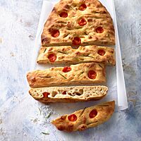 Die mit halbierten Kirschtomaten und Rosmarinnadeln belegte, goldgelb ausgebackene Focaccia hat eine lockere, mittelporige Krume.