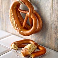 Die Laugenbrezeln mit glänzender Oberfläche und dünnen Ärmchen sind am Bauch eingeschnitten und mit grobem Salz bestreut.