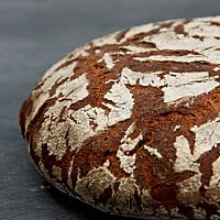 Die bemehlte Kruste des runden Roggenbrotlaibes hat breite, dunkle Risse auf der weißen Oberfläche.
