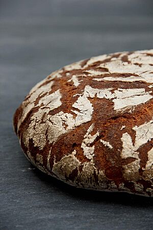 Die bemehlte Kruste des runden Roggenbrotlaibes hat breite, dunkle Risse auf der weißen Oberfläche.