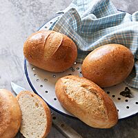 Das goldbraun ausgebackene Rheinische Schnittbrötchen mit glänzender, eingeschnittener und rustikal aufgerissener Kruste (unten) liegt neben zwei Hamburger Rundstücken.