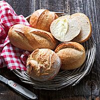 Ein knusprig ausgebackenes, rundes Mütschli mit weitem Ausbund (oben) liegt neben einem Pariserli (links), einem Glarner Brötli (rechts) sowie einem Schlumbergerli (unten) in einem geflochtenem Brotkorb.