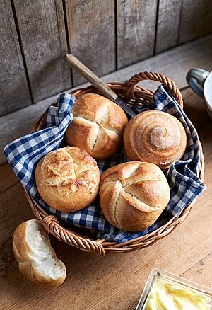 Das runde, kräftig ausgebackene Joghurtbrötchen mit spiralförmigem Ausbund (rechts oben) liegt neben einer Münchener Mundsemmel (links oben) sowie einer Rosensemmel (links unten) und einer Kaisersemmel (rechts unten) in einem geflochtenen Brotkorb.