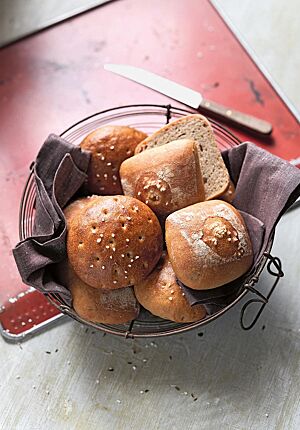 In einem mit einem braunen Tuch ausgelegten Drahtkorb liegen Berliner Salzkuchen in der Ost- (links) und Westvariante (rechts). Die runden Ost-Salzkuchen haben eine glatte, glänzende, gestippte und mit grobem Salz bestreute Kruste.