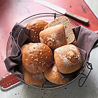 In einem mit einem braunen Tuch ausgelegten Drahtkorb liegen Berliner Salzkuchen in der Ost- (links) und Westvariante (rechts). Die eckigen West-Salzkuchen haben eine glatte, glänzende Kruste mit grobem Salz in der Mitte.
