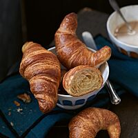 Pariser Gipfel (oben rechts), Bamberger Hörnla (unten) und Croissants (oben links) liegen in einem weißen Schälchen. Die Croissants haben eine goldbraun ausgebackene, glänzende Kruste und eine feinblättrige, buttrige Krume.