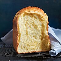 Eine an der Kontaktstelle auseinandergebrochene Brioche liegt auf einem dunklen Gitterrost. Die helle, wattige Krume wird von einer feinen Krume umgeben.