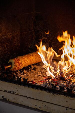 Ein um eine Holzstange gewickelter Skalický Trdelník wird nahe einer offenen Flamme gebacken.