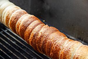 Trdelník auf Sauerteigbasis. Der vor dem Backen in Zucker gewälzte Sauerteig-Trdelník hat eine goldbraun ausgebackene und glänzende Oberfläche.