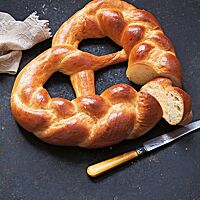 Eine aus drei Strängen geflochtene Brezel mit glatter, glänzender Kruste liegt auf einer dunklen Platte. Die wattig-weiche Krume hat eine ungleichmäßige Porung.