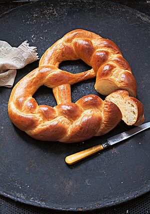 Eine aus drei Strängen geflochtene Brezel mit glatter, glänzender Kruste liegt auf einer dunklen Platte. Die wattig-weiche Krume hat eine ungleichmäßige Porung.