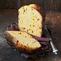 Zwei Panettonehälften liegen auf einem dunklen, lilafarbenen Tuch auf einer Drahtschale. Die Krume des Panettone ist luftig und locker und von Sultaninen und Orangeat durchzogen. Die Kruste des in einer Papierform gebackenen Panettone ist dunkelbraun ausgebacken.
