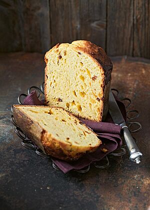 Zwei Panettonehälften liegen auf einem dunklen, lilafarbenen Tuch auf einer Drahtschale. Die Krume des Panettone ist luftig und locker und von Sultaninen und Orangeat durchzogen. Die Kruste des in einer Papierform gebackenen Panettone ist dunkelbraun ausgebacken.