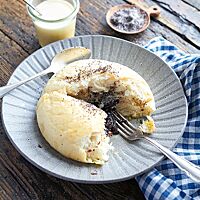 Ein aufgerissener Riesengermknödel liegt auf einem grauen, tiefen Teller. Im Inneren wird die Pflaumenmusfüllung sichtbar, die von der hellen, wattigen Krume umgeben ist.