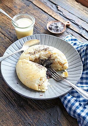 Ein aufgerissener Riesengermknödel liegt auf einem grauen, tiefen Teller. Im Inneren wird die Pflaumenmusfüllung sichtbar, die von der hellen, wattigen Krume umgeben ist.