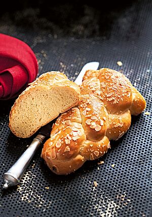 Der angeschnittene Schweizer Dinkelzopf hat eine goldbraun ausgebackene, feine Kruste die mit Mandelblättchen bestreut ist. Die kleinporige Krume ist elastisch und faserig.