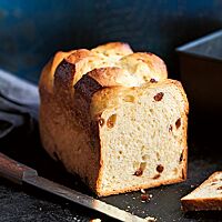 Vor der angeschnittenen Taillaule, die in einer Kastenform gebacken wurde, liegt ein Brotmesser auf dunklem Untergrund. In der elastischen, hellen Krume sind vereinzelt Sultaninen sichtbar.