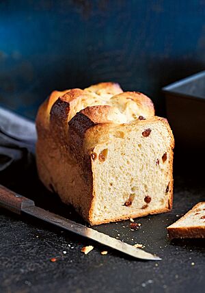 Vor der angeschnittenen Taillaule, die in einer Kastenform gebacken wurde, liegt ein Brotmesser auf dunklem Untergrund. In der elastischen, hellen Krume sind vereinzelt Sultaninen sichtbar.