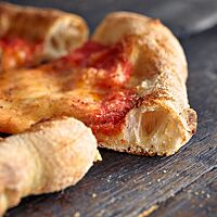 Im Anschnitt zeigt die mit Tomatensauce und Mozzarella belegte Pizza den knusprig ausgebackenen Rand mit der grobporige Krume.
