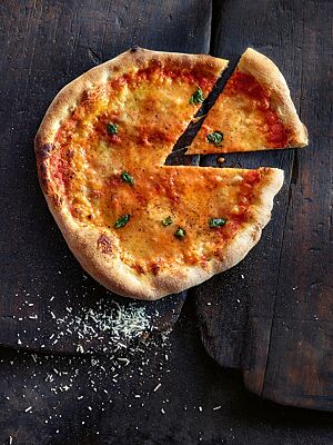 Eine mit Tomatensauce, Mozzarella und Basilikum belegte Pizza Margherita zeigt ihren hellbraun ausgebackenen, knusprigen Rand.