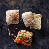 Die hellbraun ausgebackenen Pizzabrötchen haben eine glatte, leicht bemehlte Kruste und eine kleinporige, lockere Krume. Ein halbiertes Pizzabrötchen wurde als Bruschetta mit würzigem Tomatensalat belegt.
