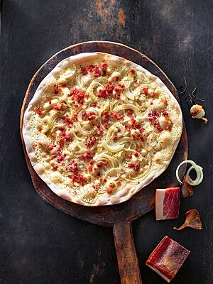 Der knusprig ausgebackene klassische Flammkuchen ist mit Crème fraîche, Bauchspeck und Zwiebeln belegt.
