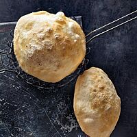 Zwei knusprig frittierte, aufgeblähte Bhatura zeigen ihre goldgelbe Kruste.