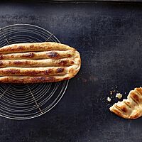 Das längliche, mit Hefe gelockerte Tanoori-Fladenbrot hat eine goldgelb ausgebackene Kruste mit goldbraunen Stellen und tiefen länglichen Furchen sowie eine lockere, elastische Krume.
