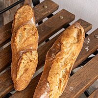 Zwei Dinkelbaguettes mit weit geöffnetem Ausbund liegen auf einem Holzstuhl.