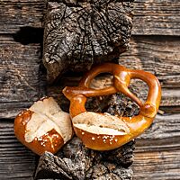 Goldbraun ausgebacken lehnen eine Laugenbrezel und ein Laugenbrötchen an einer rustikalen Holzwand.