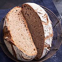 Das halbierte Weizenvollkornbrot liegt mit der Schnittfläche nach oben in einem Brotkorb. Die kleinporige, elastische Krume ist von der bemehlten, knusprigen, rustikal aufgerissenen Kruste umgeben.