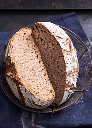 Das halbierte Weizenvollkornbrot liegt mit der Schnittfläche nach oben in einem Brotkorb. Die kleinporige, elastische Krume ist von der bemehlten, knusprigen, rustikal aufgerissenen Kruste umgeben.