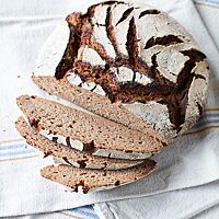 Das Roggenvollkornbrot hat eine lockere, saftige Krume und eine stark bemehlte Kruste, die mit den dunklen Rissen auf der Oberfläche kontrastiert.