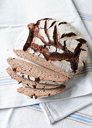 Das Roggenvollkornbrot hat eine lockere, saftige Krume und eine stark bemehlte Kruste, die mit den dunklen Rissen auf der Oberfläche kontrastiert.