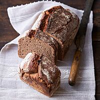 Der in der Kastenform kräftig ausgebackene Braunbär liegt angeschnitten auf einem weißen Tuch. Rechts neben dem Brot liegt ein rustikales Brotmesser.