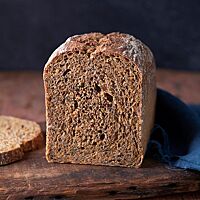 Der angeschnittene Wurzelkasten liegt auf einem dunklen Holzbrett. Die dunkle, saftige Krume ist von einer feinen Kruste umgeben.