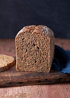 Der angeschnittene Wurzelkasten liegt auf einem dunklen Holzbrett. Die dunkle, saftige Krume ist von einer feinen Kruste umgeben.