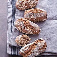 Die mit Haferflocken bestreuten Müslaner liegen auf einem grauen Tuch. Ein auseinandergebrochenes Brötchen zeigt die elastische, saftige, kleinporige Krume.