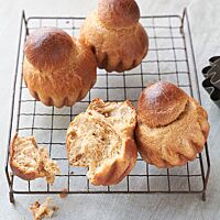 Goldbraun ausgebackene, glänzende Brioches liegen auf einem Gitterrost. Eine auseinandergebrochene Brioche zeigt die wattige, fluffige Krume.