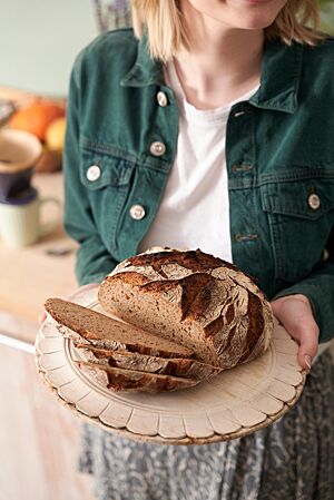 Ein Roggenmischbrot liegt mit mehreren abgeschnittenen Scheiben auf einem Holztablett. Die lockere, kleinporige Krume ist umgeben von einer rustikal aufgerissenen, kräftig ausgebackenen Kruste.