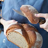 Das angeschnittene Weizenmischbrot mit Kartoffel hat eine lockere, weiche Krume und eine goldbraun ausgebackene, bemehlte Kruste mit einer kreuzförmigen Einkerbung auf der Oberseite.