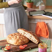 Auf einem Holzbrett liegt das angeschnittene Fladenbrot mit goldgelber Kruste und mittelporiger, lockerer Krume.