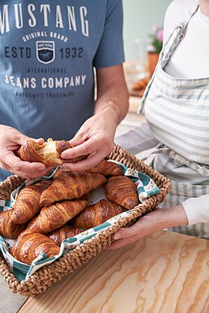 In einem Flechtkorb liegen mehrere goldbraun ausgebackene, glänzende Croissants. Eines davon wird auseinandergezogen und lässt die wattige, sehr elastische Krume erkennen.